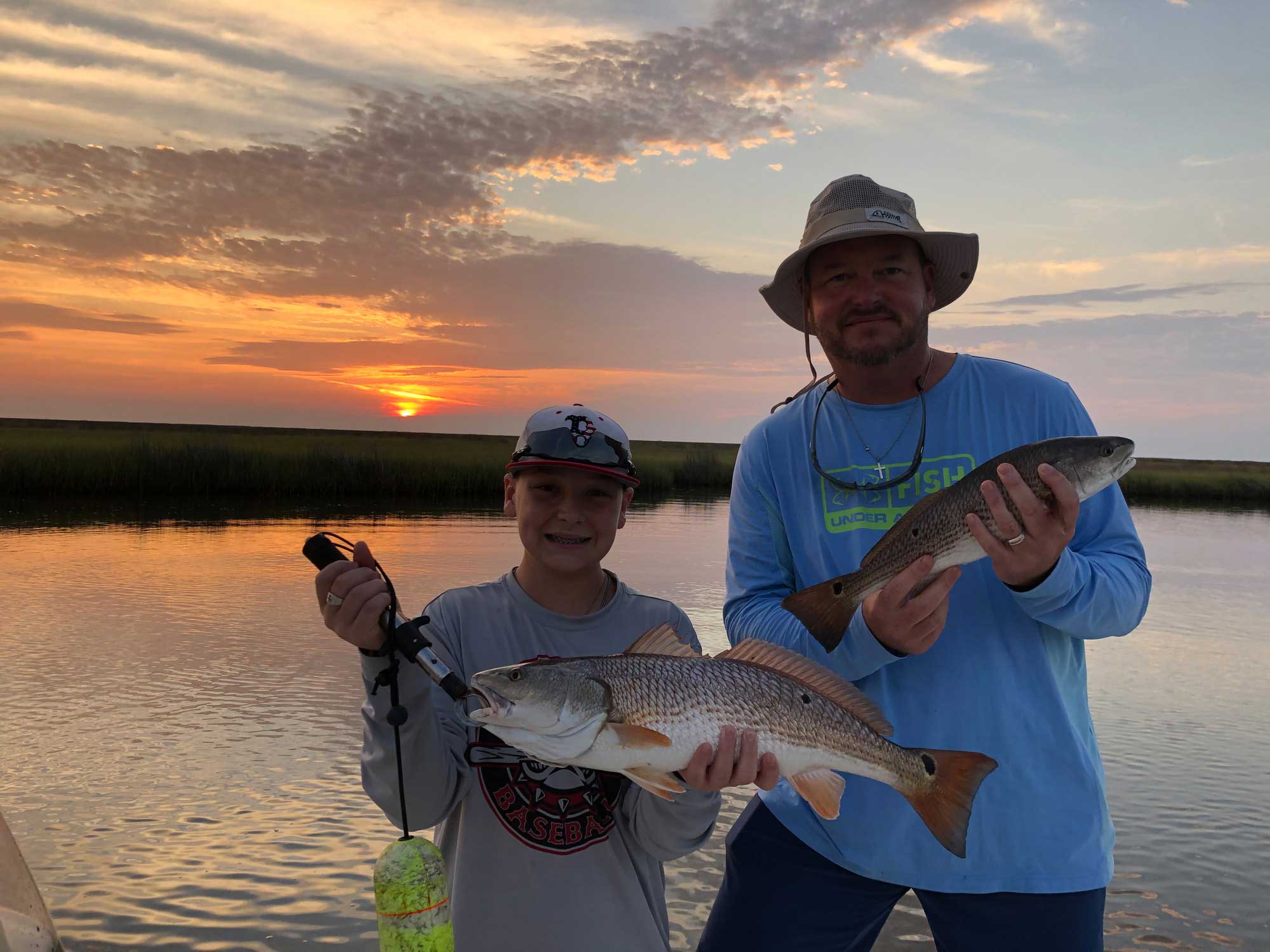 father and son holding two redfish during sunset in new orleans