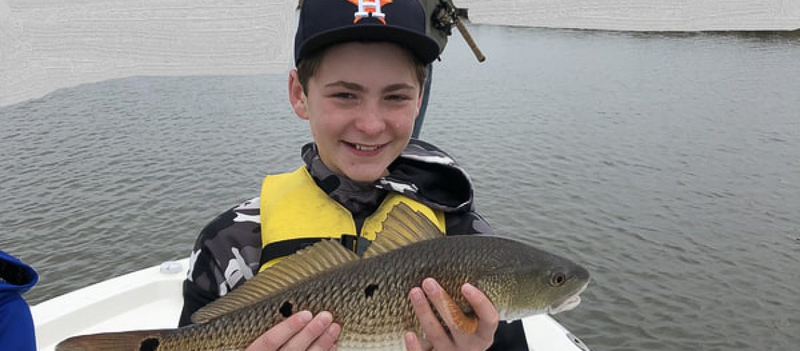 boy holding a medium size redfish on lake